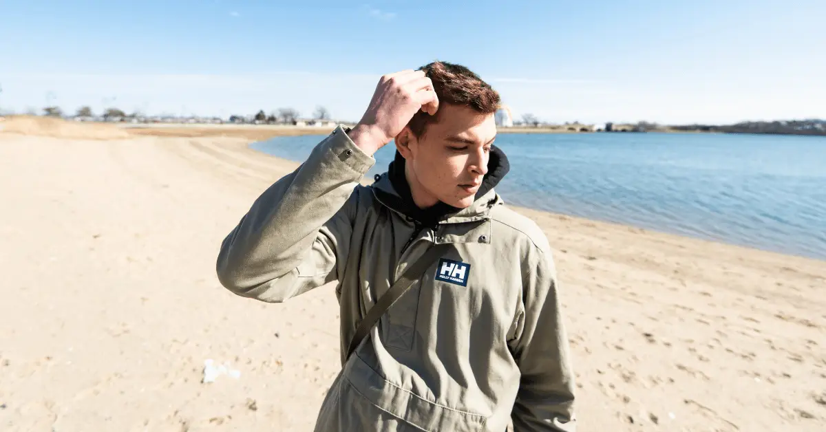 A young man wearing a jacket standing on the beach.