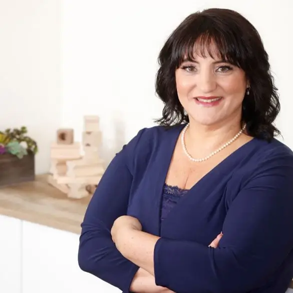 A woman with her arms crossed in front of a kitchen.