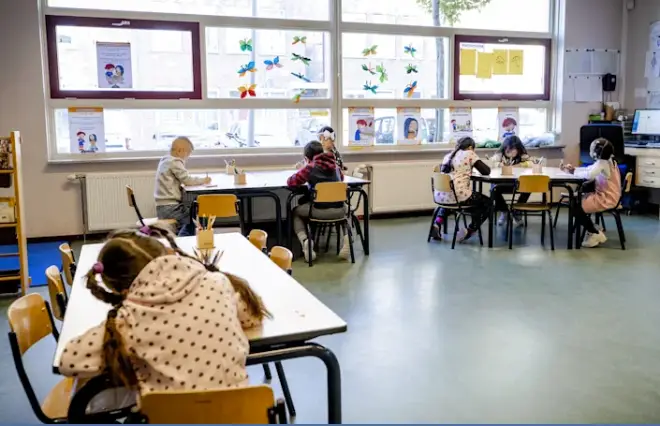 A group of children sitting at tables in a classroom creating a media kit.
