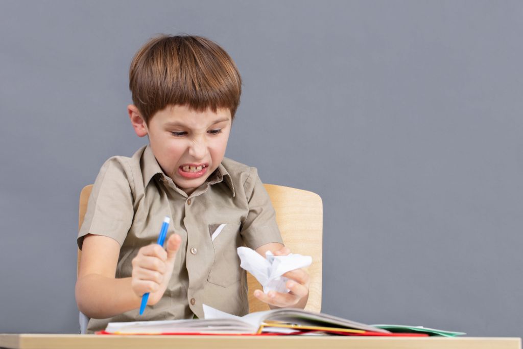 "A frustrated child sitting at a desk with a book and pen, showing signs of typical moodiness—furrowed brow, clenched jaw, and slumped posture—struggling with homework or school-related stress.