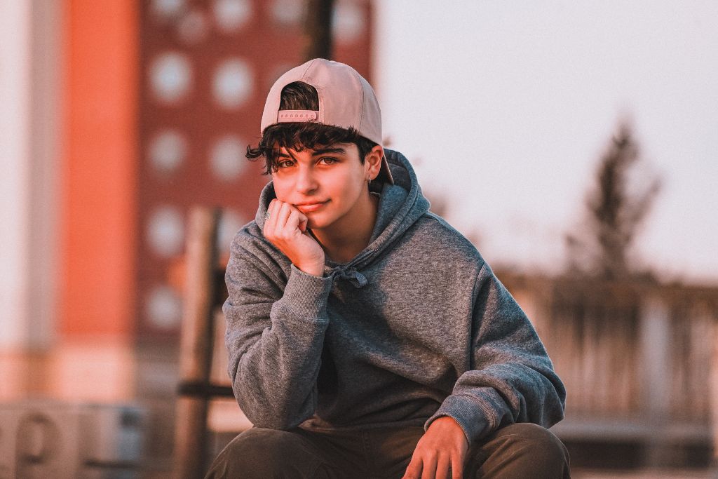 Teenage boy in a hoodie and cap sitting outdoors, reflecting quietly—capturing the emotional journey of teen relationships